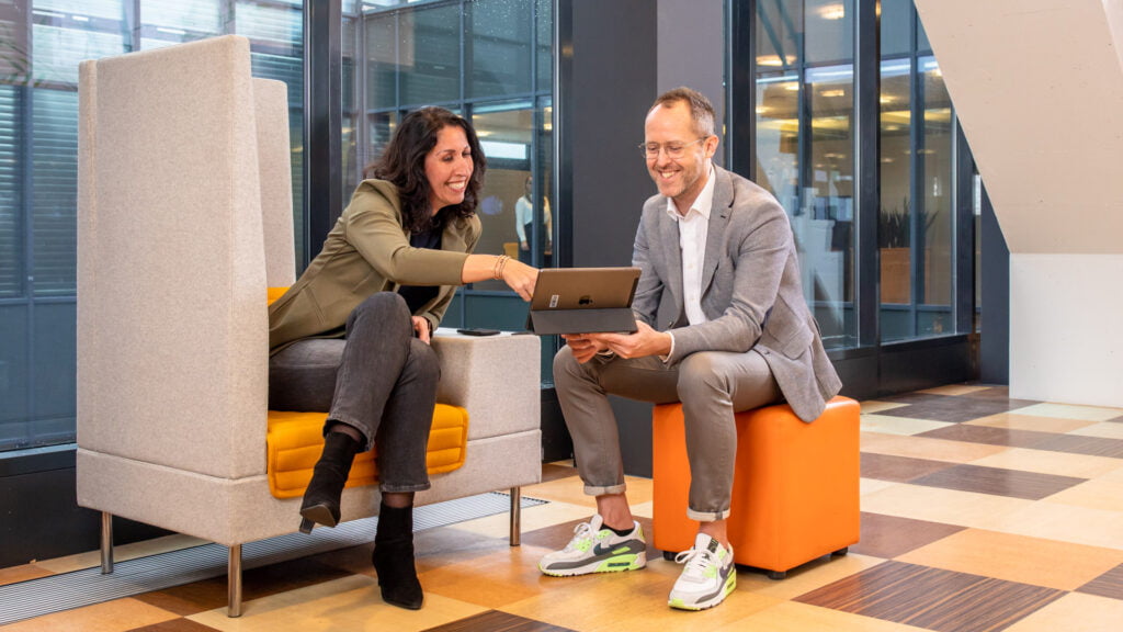 Twee medewerkers zittend in overleg waarbij een medewerker de andere medewerker iets aanwijst op de iPad.